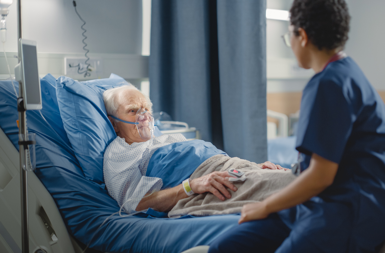 Patient receiving oxygen in hospital with nurse or clinician sitting nearby