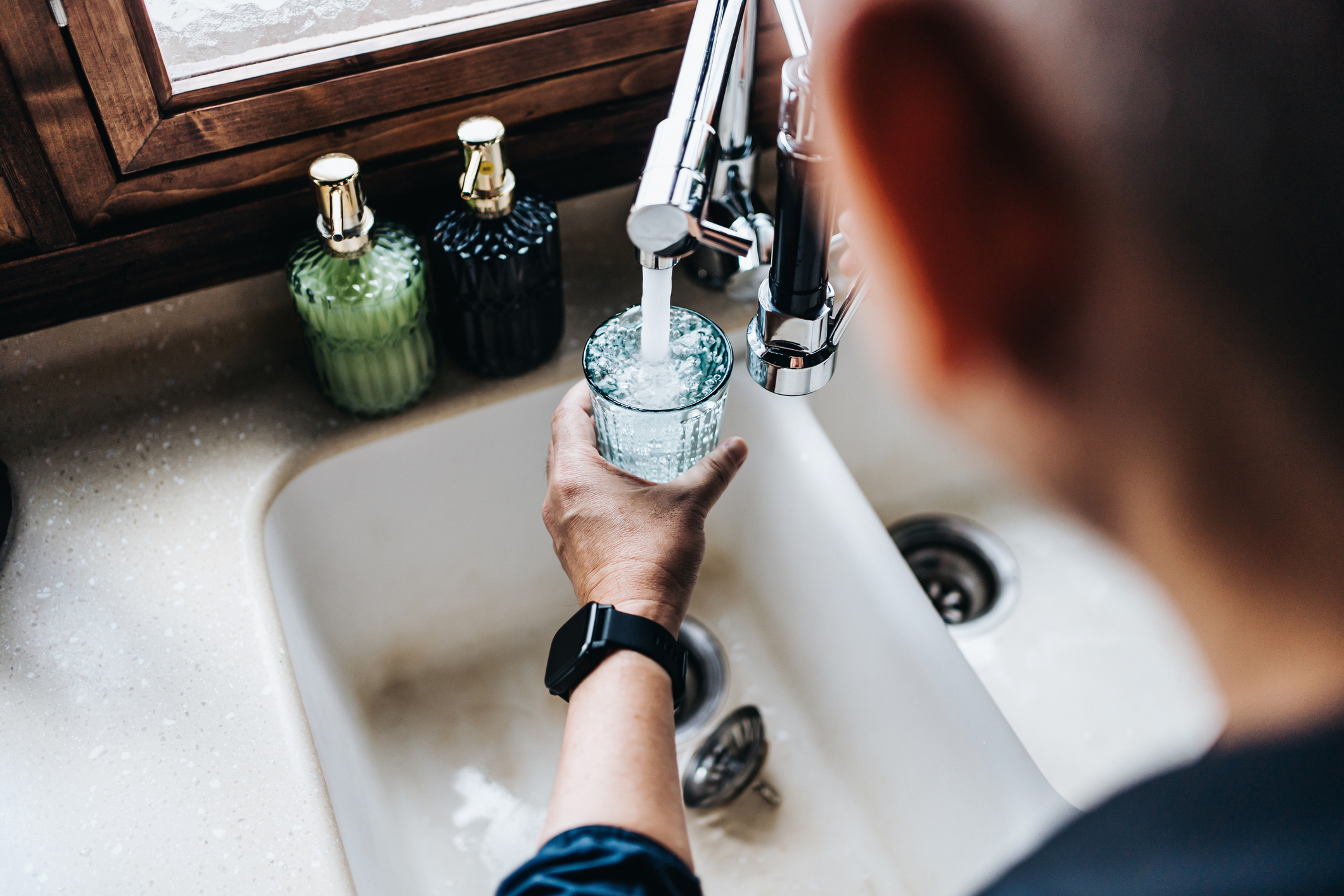 Person filling glass with drinking water at sink